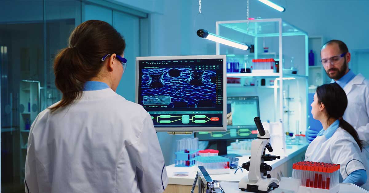 Alcuni medici lavorano in un laboratorio moderno. Su uno schermo sono visibili dati sanitari complessi a simboleggiare come le ultime innovazioni mediche abbiano un forte impatto sulla gestione delle cure.