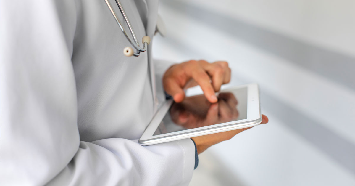 Un medico utilizza un tablet, simboleggiando l’adozione della digitalizzazione nella sanità, determinata a superare le sfide tecnologiche e di budget.